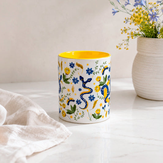 Taza sublimada de 325ml Encanto de Serpiente con asa e interior amarillo, diseño místico de serpientes azules, flores, hojas y detalles dorados.