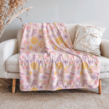 Manta de invierno celestial con diseño de lunas, soles, estrellas y cristales en tonos pastel, confeccionada en felpa con reverso sherpa blanco.