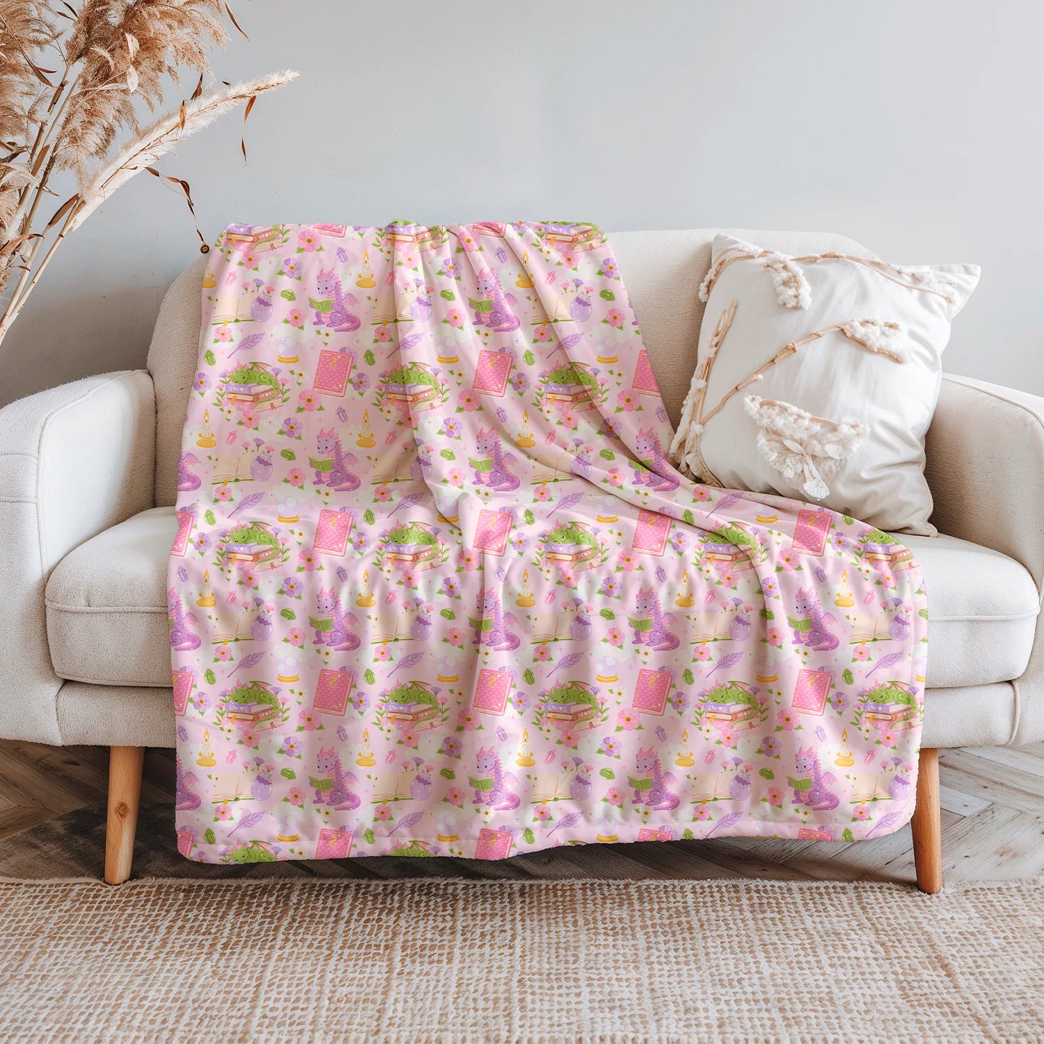 Manta literaria con diseño de dragones lectores, libros y flores en tonos rosados, confeccionada en felpa con reverso sherpa blanco.