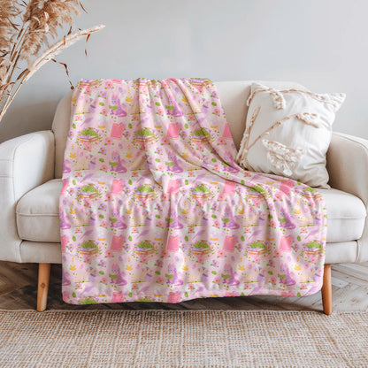 Manta literaria con diseño de dragones lectores, libros y flores en tonos rosados, confeccionada en felpa con reverso sherpa blanco.