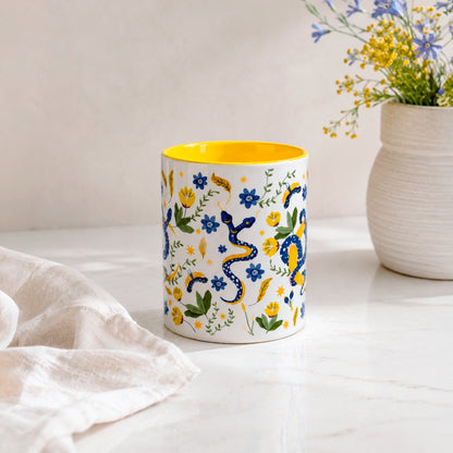 Taza sublimada de 325ml Encanto de Serpiente con asa e interior amarillo, diseño místico de serpientes azules, flores, hojas y detalles dorados.