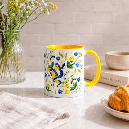 Taza sublimada de 325ml Encanto de Serpiente con asa e interior amarillo, diseño místico de serpientes azules, flores, hojas y detalles dorados.