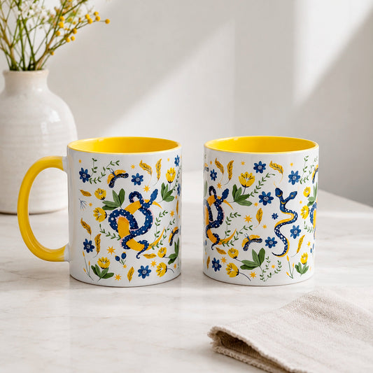 Taza sublimada de 325ml Encanto de Serpiente con asa e interior amarillo, diseño místico de serpientes azules, flores, hojas y detalles dorados.